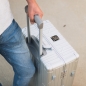 Preview: Nahaufnahme einer Person in Jeans, die einen silbernen GUNDEL Koffer am Teleskopgriff hält.