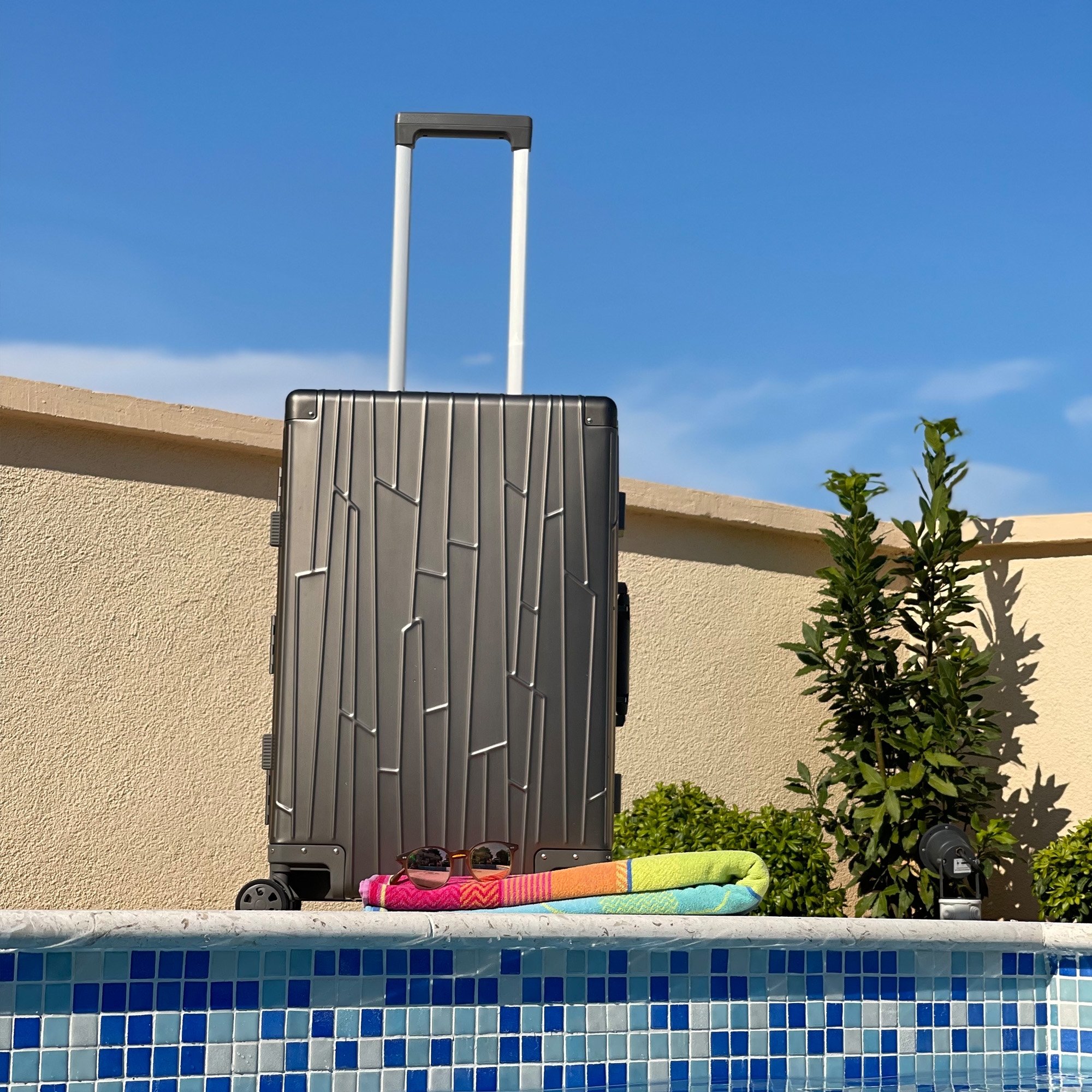 GUNDEL Space Grey Koffer mit Teleskopgriff steht neben einem Pool mit blauem Mosaikrand.